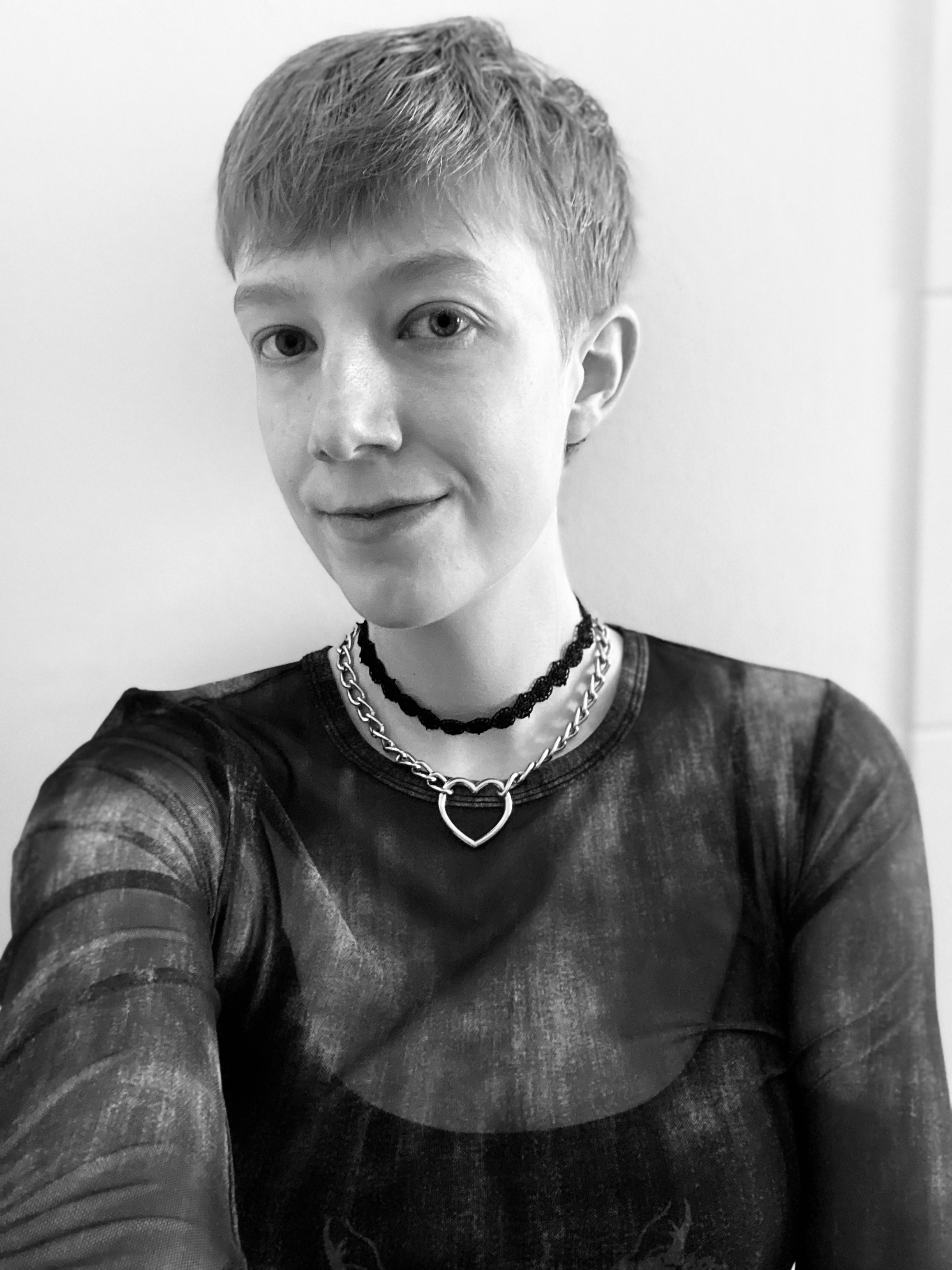 a black and white photo of me, a white non-binary person with short hair wearing a mesh shirt over a black crop top, and a black choker.